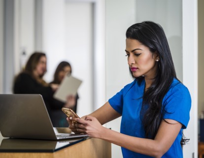 Female doctor with smart phone and laptop at reception desk