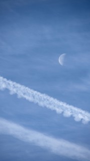 Airplane contrails and waning moon against blue sky