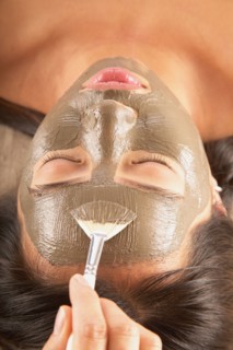 Woman with mud mask and cucumbers on face