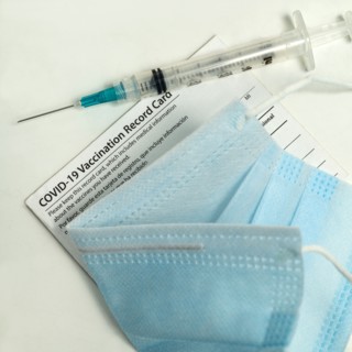 Syringe on Covid-19 vaccination record card and face mask