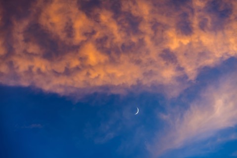 Crescent moon against blue sky with pink and orange clouds