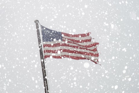 Torn American flag on flag pole with falling snow