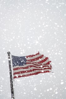 Torn American flag on flag pole with falling snow