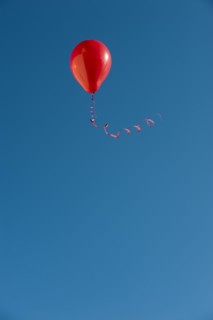 Red balloon with ribbon flying against blue sky