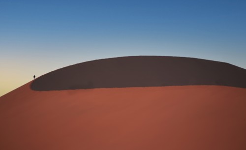 Lone man climbing giant sand dune