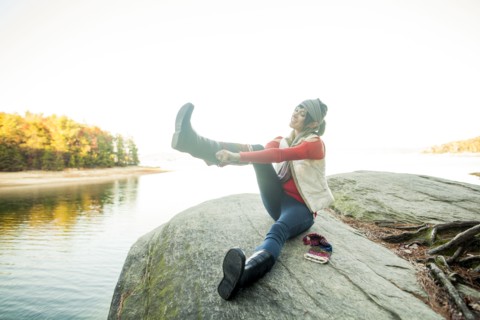 Caucasian woman pulling on boots near lake