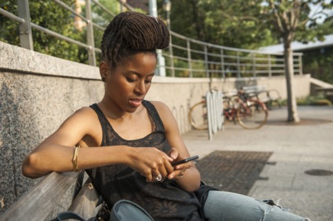 African American woman on bench at park texting on cell phone