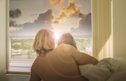 Caucasian couple in bed watching sunset at window