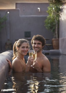 Smiling Caucasian couple toasting with champagne in swimming pool