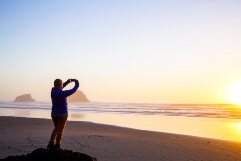 Caucasian woman taking picture of sunrise on beach