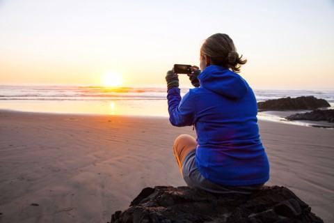 Caucasian woman taking picture of sunrise on beach
