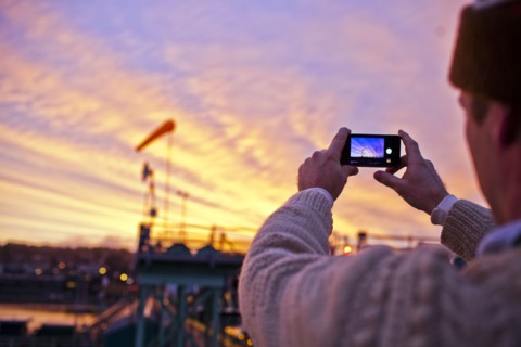 Man taking picture of sunset over bridge