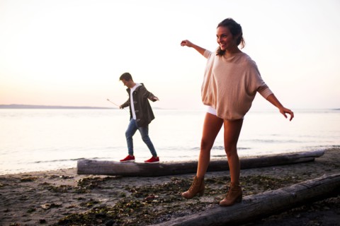 Caucasian couple walking on logs on beach