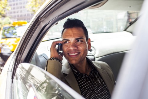 Hispanic businessman talking on cell phone in back seat of car