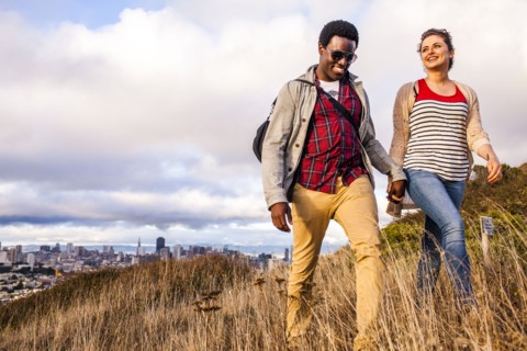 Couple walking on grassy hill overlooking cityscape