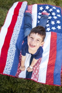 Mixed race boy laying on American flag blanket on grass