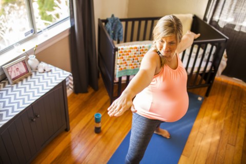 Pregnant Caucasian woman practicing yoga in nursery