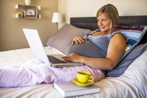 Pregnant Caucasian woman using laptop in bed