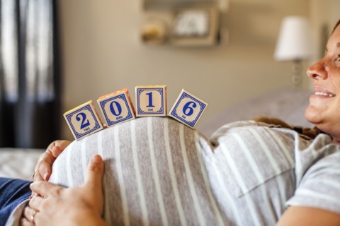Pregnant Caucasian woman balancing wooden blocks on her stomach in bed
