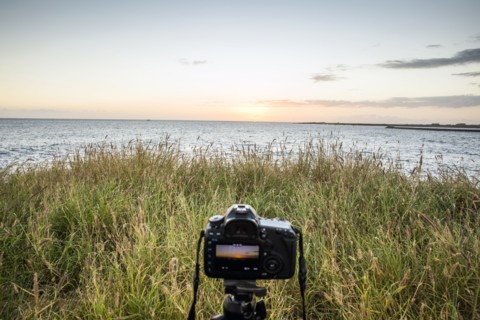 Close up of camera photographing sunset over ocean horizon