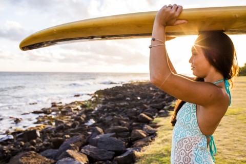 Pacific Islander surfer carrying surfboard on rocky beach