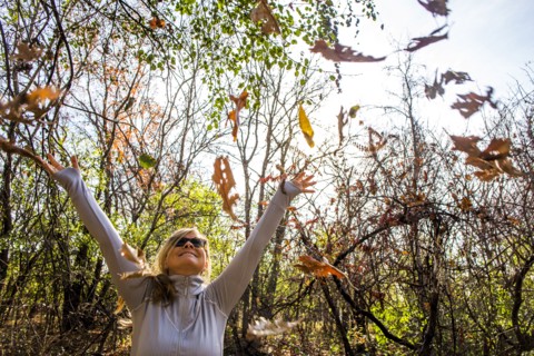 Caucasian woman throwing autumn leaves in forest