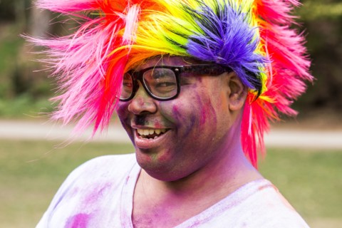 Smiling man covered in pigment powder wearing multicolor wig