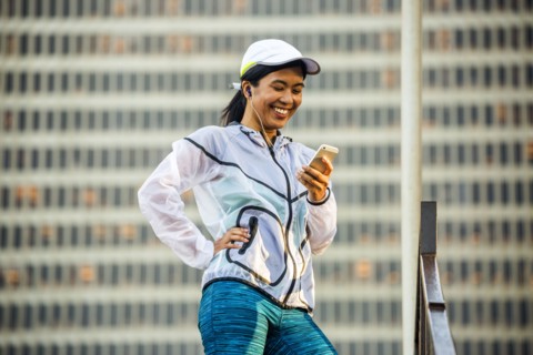 Asian runner using cell phone near highrise building