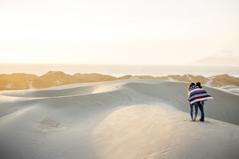 Mixed race women wrapped in blanket in sand dunes