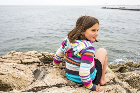 Smiling Caucasian girl sitting on rocks at ocean