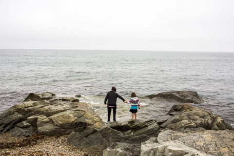 Caucasian mother and daughter holding hands on rocks at ocean