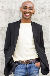 Smiling gay Black man leaning on concrete wall