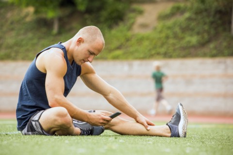 Caucasian man sitting on sports field texting on cell phone