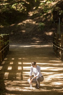 Crouching woman holding water bottle on sunny path
