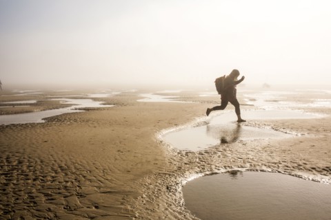 Caucasian mother carrying daughter jumping over puddle at beach