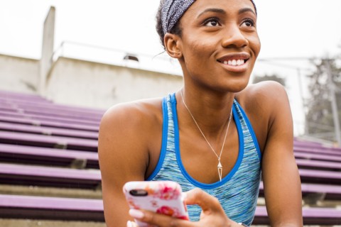Smiling Black woman sitting on bleachers texting on cell phone