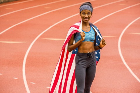Smiling Black athlete posing with American flag on track