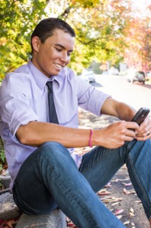 Smiling Mixed Race man sitting on curb texting on cell phone