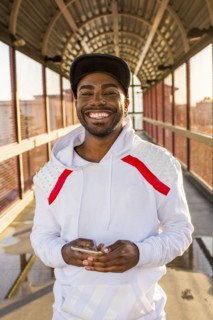 Smiling Black man holding cell phone on footbridge