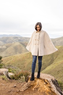 Smiling Indian woman wearing poncho standing on tree stump