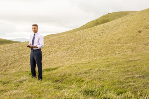 Serious Caucasian businessman standing in grass holding cell phone