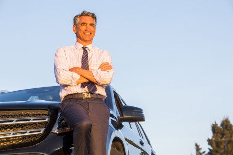 Smiling Caucasian businessman leaning on car