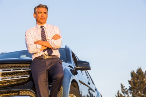 Serious Caucasian businessman leaning on car