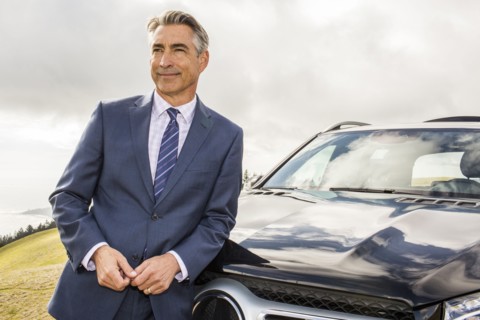 Smiling Caucasian businessman leaning on car