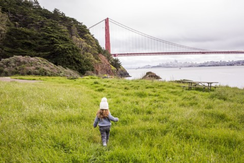 Caucasian girl walking in grass near bridge