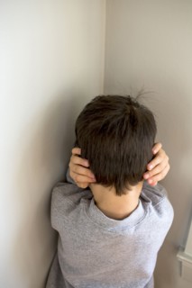 Mixed Race boy standing in corner covering ears