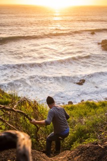 Caucasian man descending hill near ocean at sunset