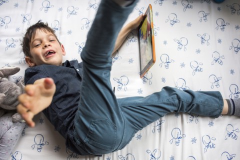 Playful Mixed Race boy laying on bed holding digital tablet