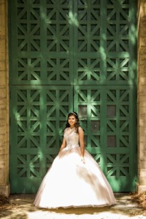 Smiling Hispanic girl wearing gown near green wall