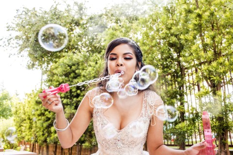 Hispanic girl wearing gown blowing bubbles